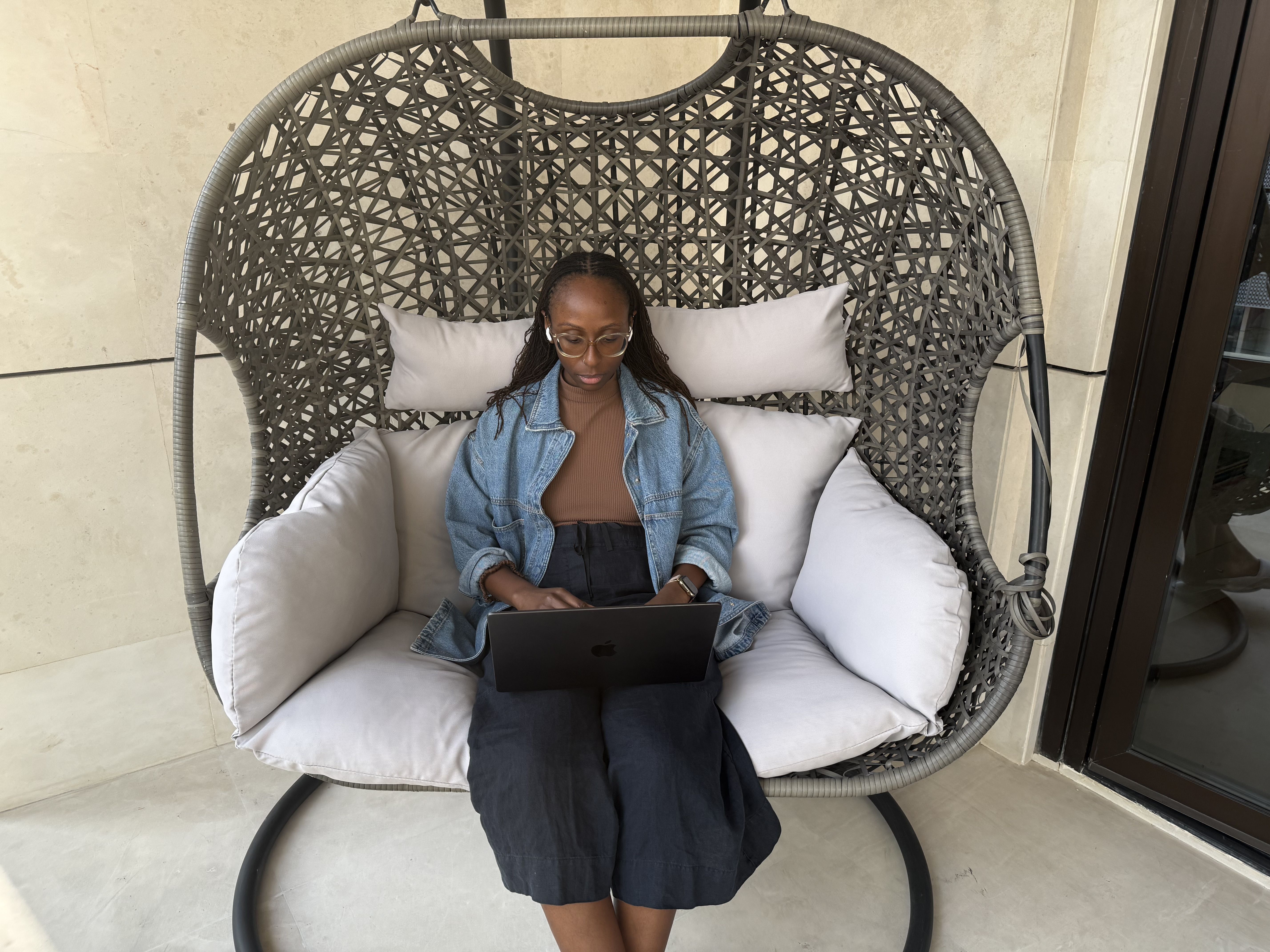 Me sitting on a hanging egg chair on my balcony, typing on my computer